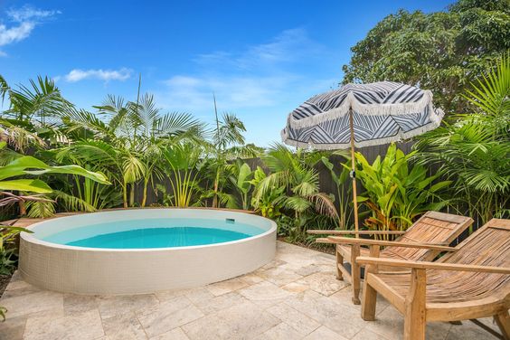 Round plunge pool set within a tropical landscape, surrounded by lush ferns and palm trees, creating a serene and exotic outdoor oasis.